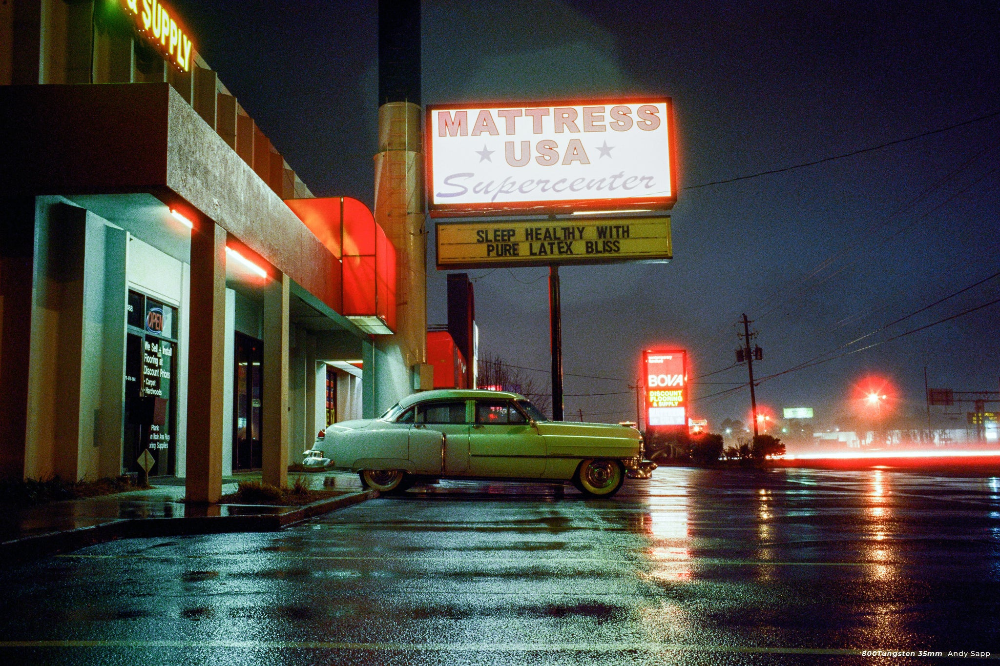 A vintage car parked in front of a neon sign at night